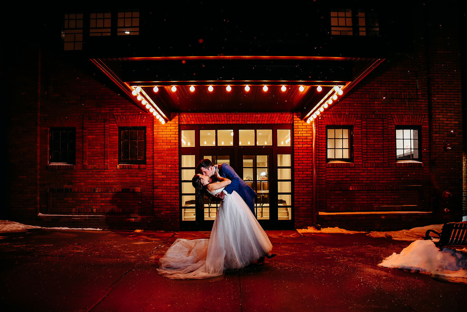 Bride and groom sharing a kiss at night underneath the Dawn Theater marquee lights
