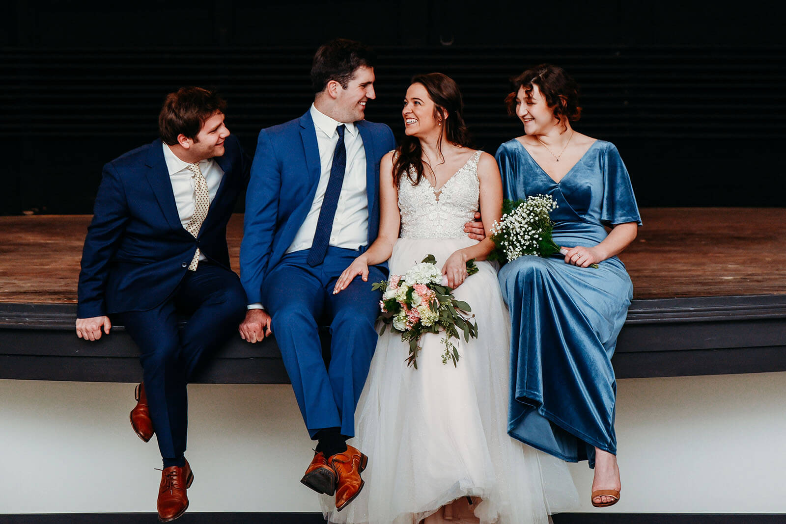 bride, groom, bridesmaid and best man smiling and sitting on the stage at the Dawn Theater